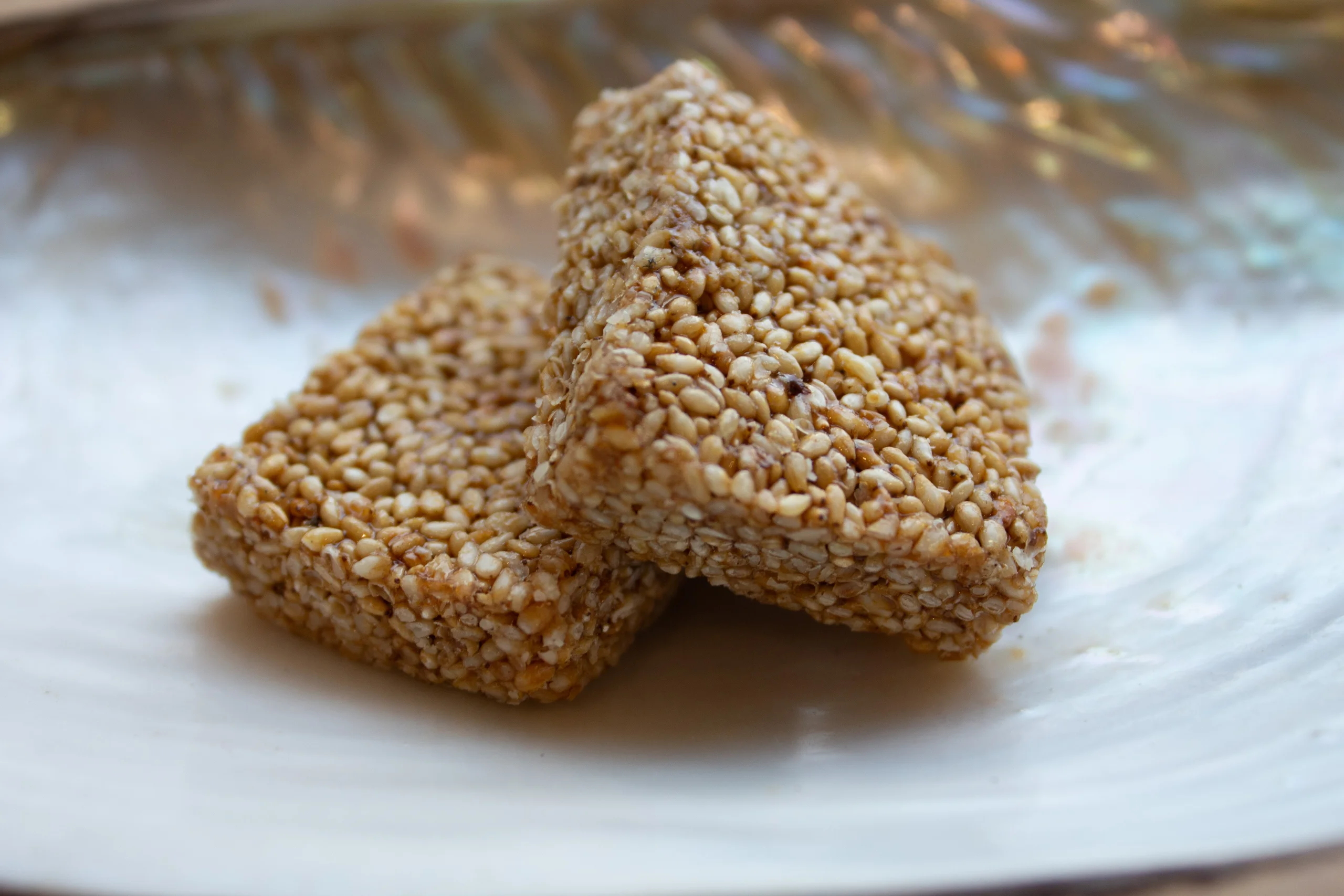 A close-up of Sesame Chikki, a traditional Indian sweet by Reddot Food, showcasing its glossy texture with golden sesame seeds bonded together with caramelized jaggery.