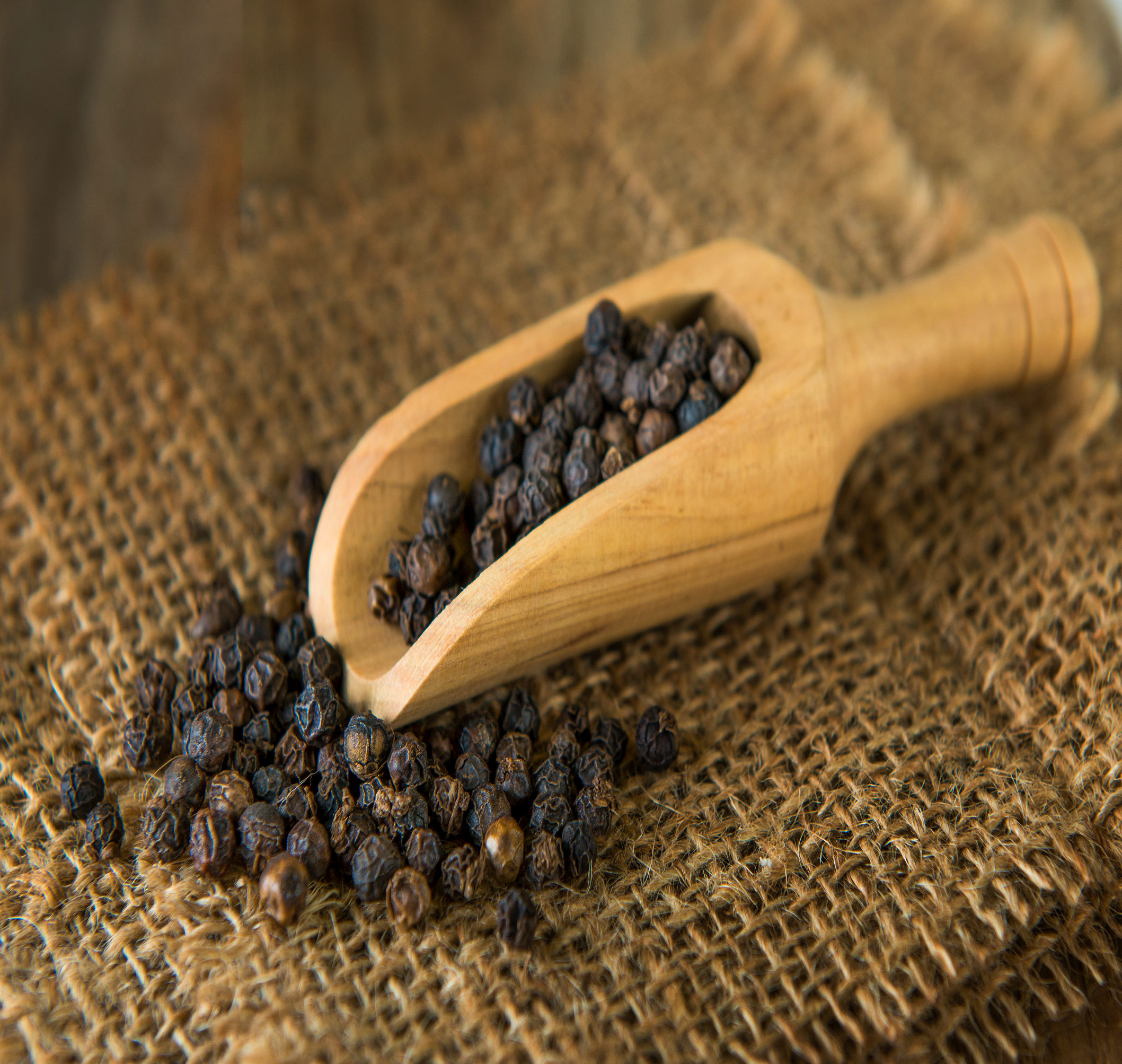 A close-up of whole black peppercorns, showcasing their dark, round, and textured appearance.